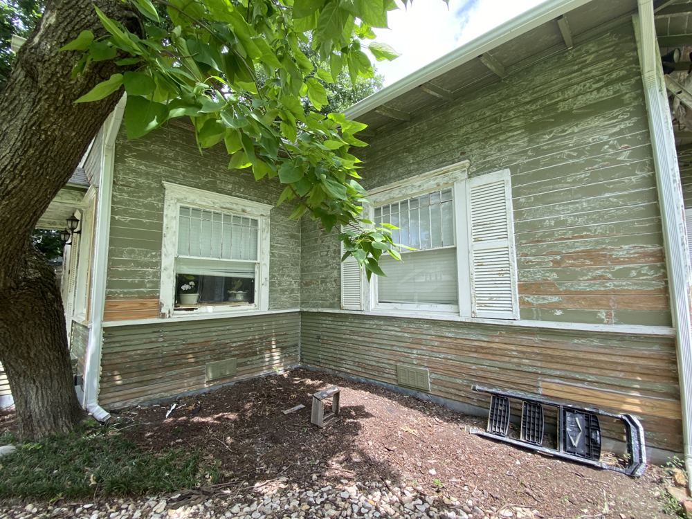 Side of a house with peeling paint and patched siding