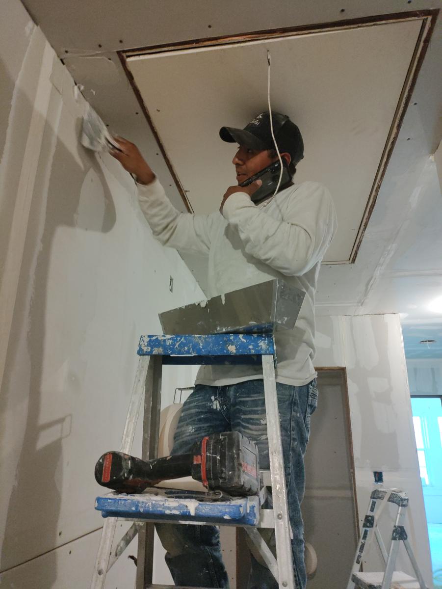 My dad on a ladder finishing new sheetrock, phone to his ear